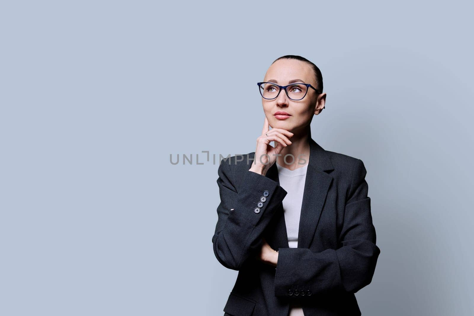 Portrait of thinking serious 30s business woman on grey studio background. Confident female in glasses suit looking to side at space for image text copy space. Business work teaching job career people