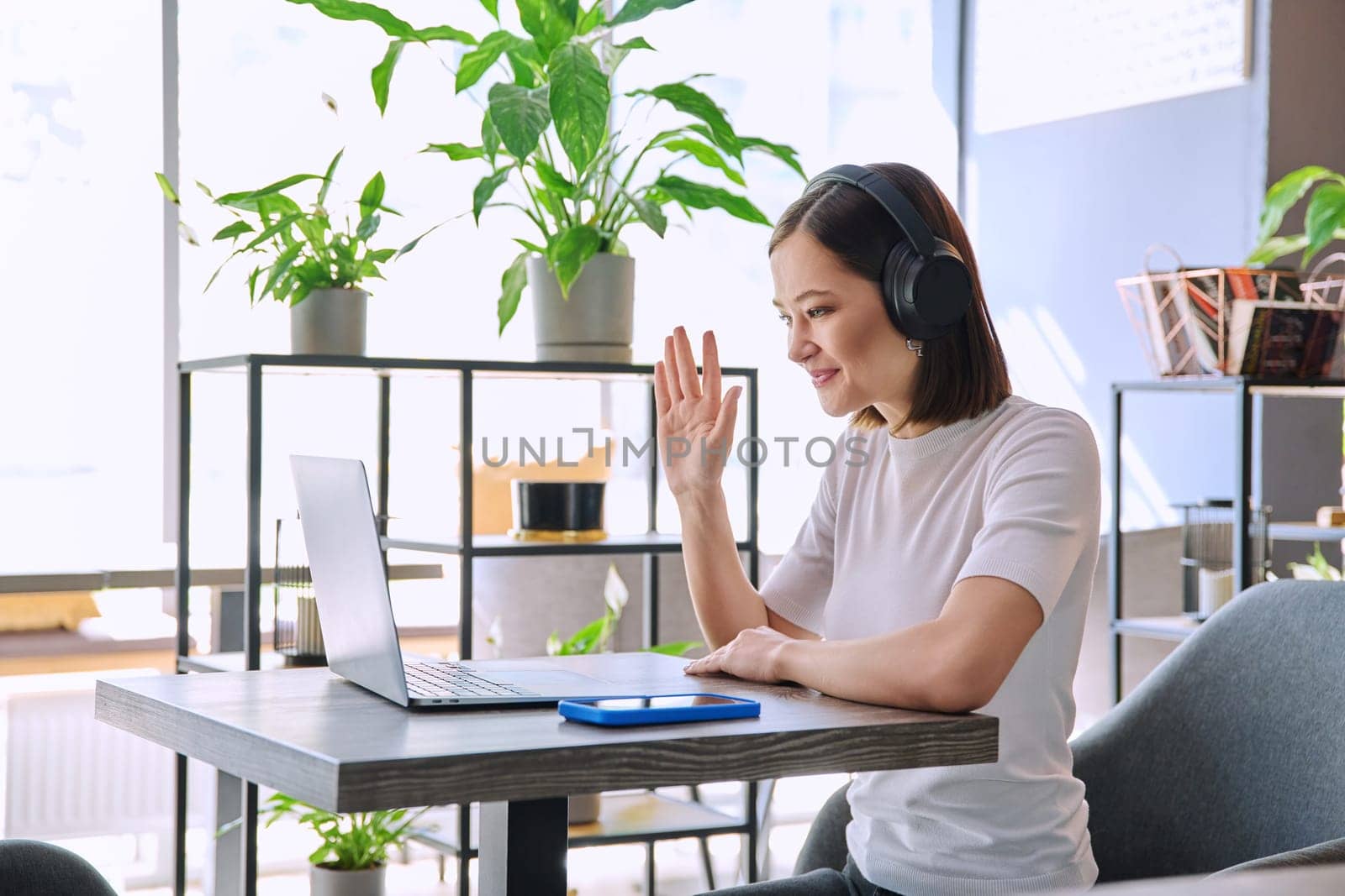 Young woman in headphones having video chat conference call using laptop computer sitting in coworking cafe. Female college student studying online listening webinar preparing exam, working remotely