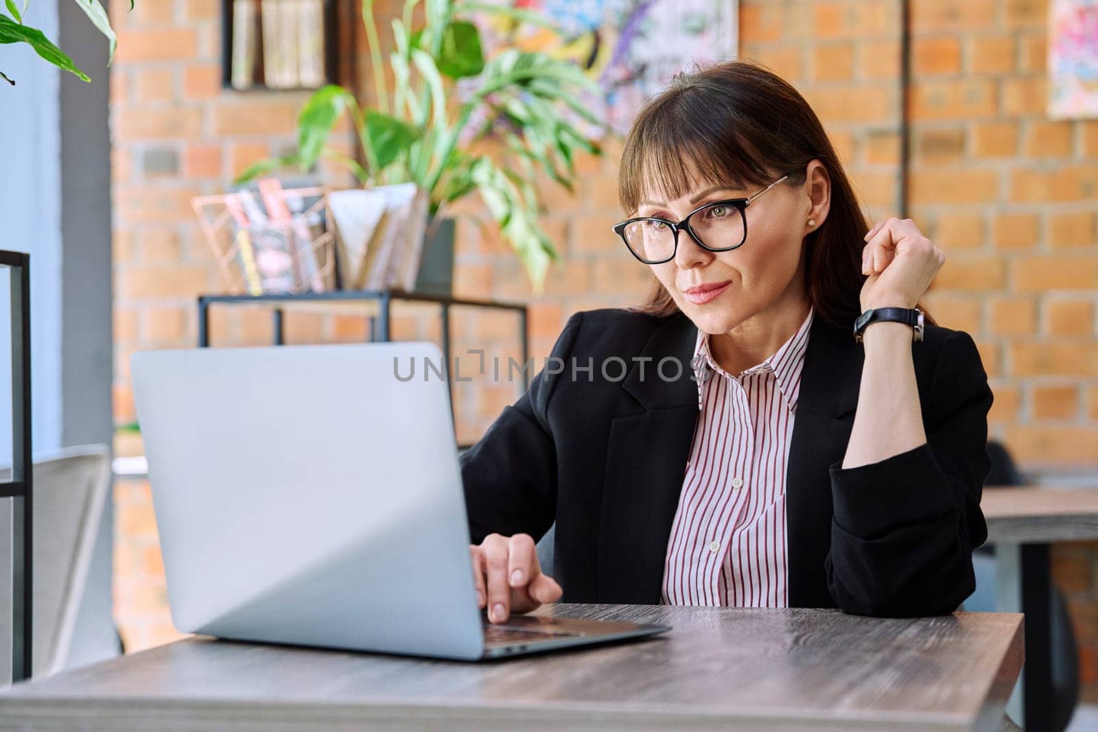 Middle-aged business confident successful serious woman working remotely at table with laptop computer in coworking cafe. Business, mature people, success, leadership, management, empowerment concept