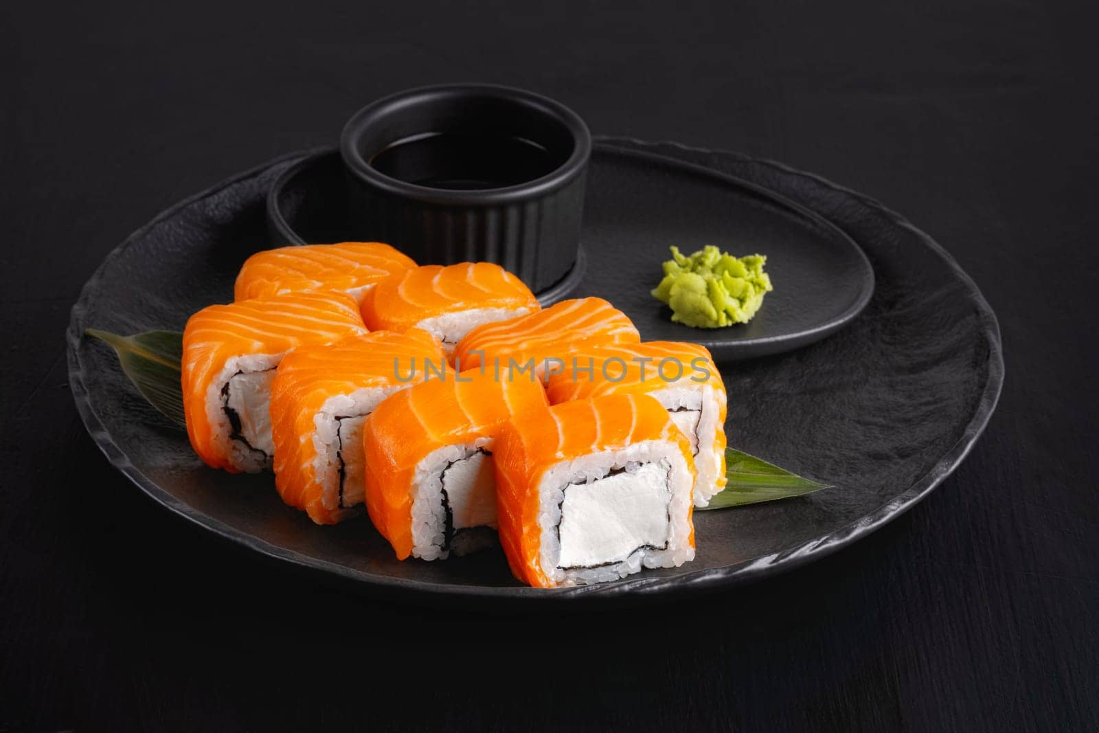 Philadelphia roll with salmon and cheese on plate on dark table.