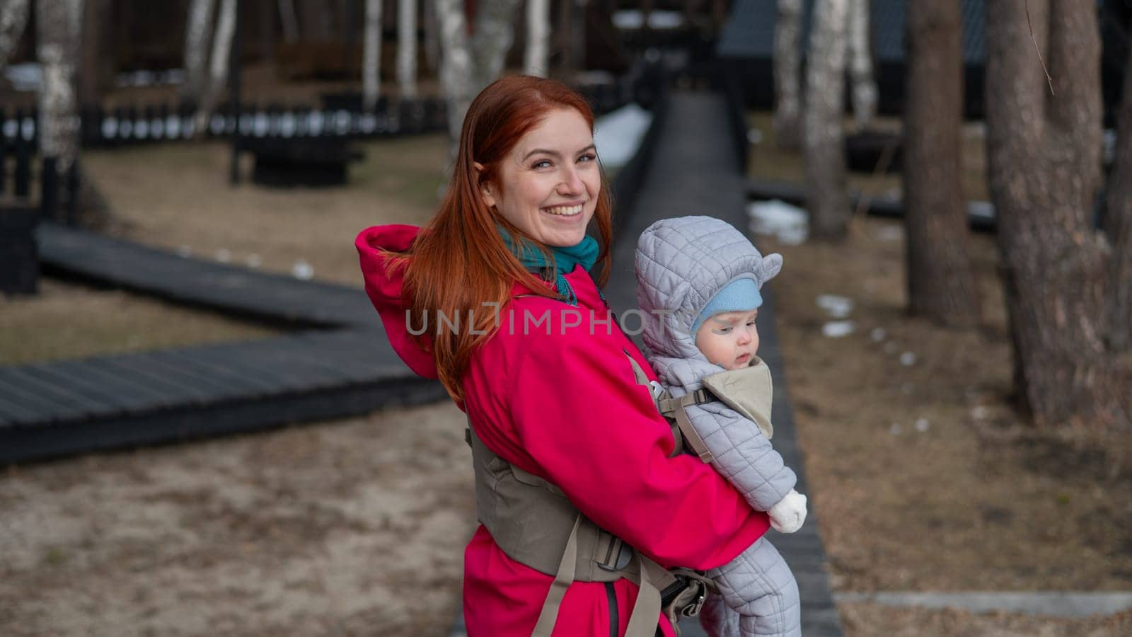 A Caucasian woman walks with her son in an ergo backpack in the countryside. by mrwed54