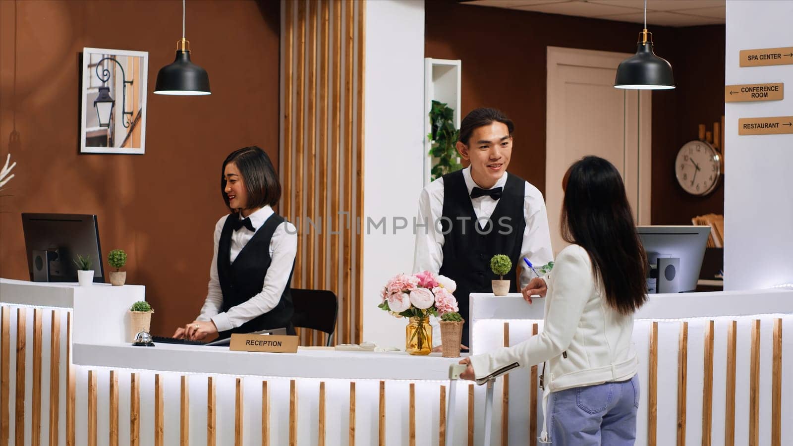 Front desk team staff welcoming hotel guest at reception, smiling and offering their concierge services to ensure pleasant relaxed stay. Employee greeting customer upon her arrival at resort.