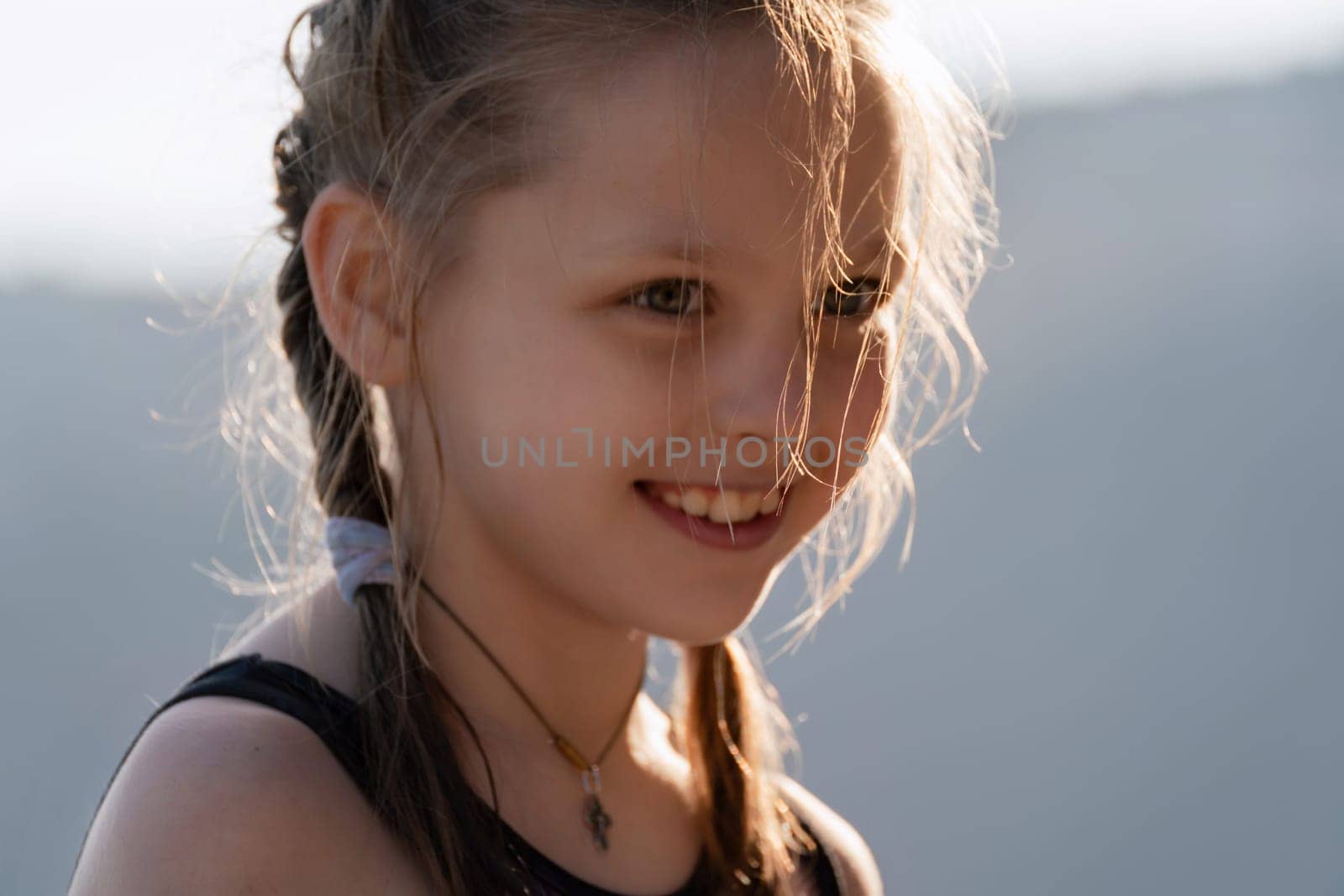 A young girl with long hair and a necklace is smiling. The necklace is a pendant with a cross on it