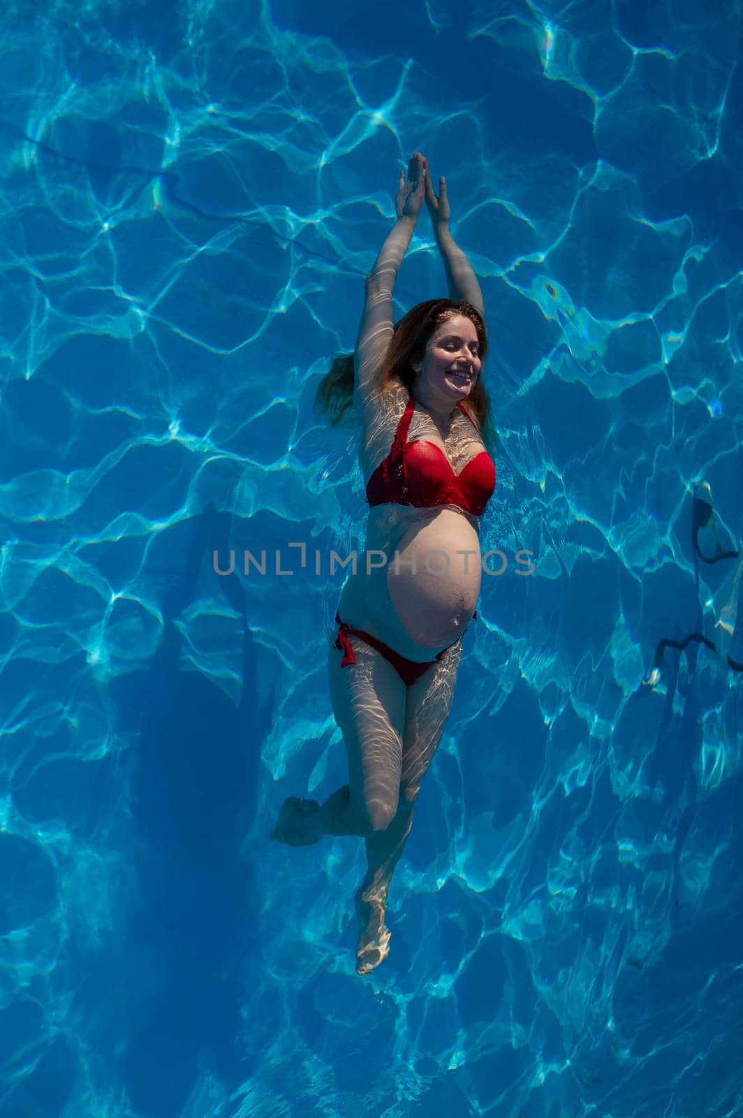 Top view of pregnant woman floating in pool in red bikini