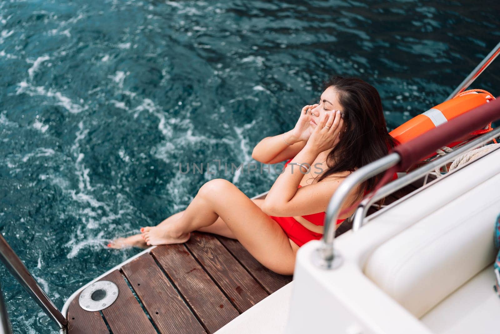 Yacht woman in a red bikini posing while on the bow of a yacht. Happy woman is sunbathing on the bow of a ship during a boat trip. Travel concept, vacation at sea.