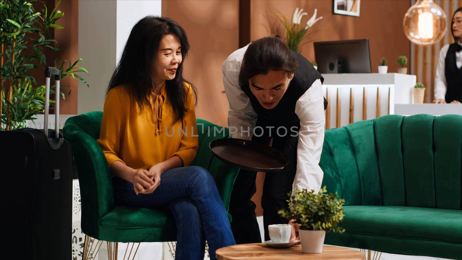 Woman paying coffee cup at pos terminal in lounge area, using credit card payment to buy drink from bar. Asian tourist finishing electronic transaction upon her arrival at hotel. Handheld shot.