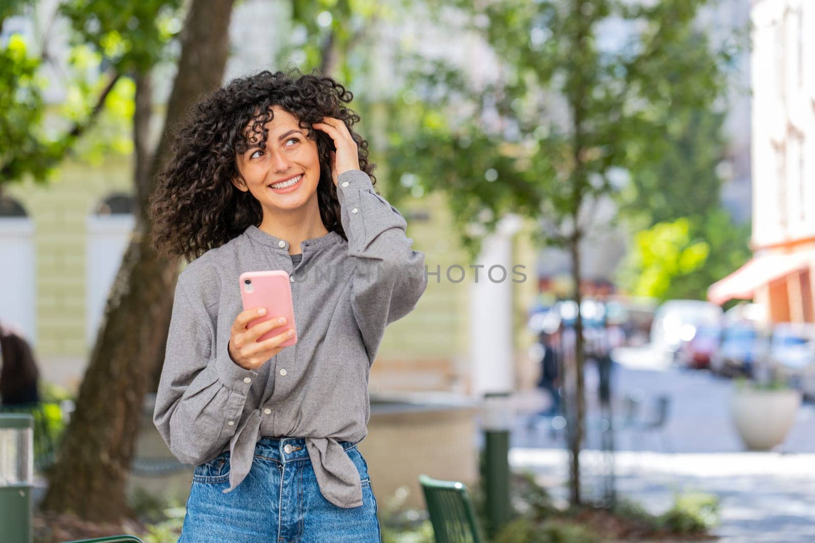 Close-up of Caucasian young woman using smartphone typing text messages in social media application online, surfing internet, relaxing, taking a break outdoors. Lady girl on city street. Sunny park