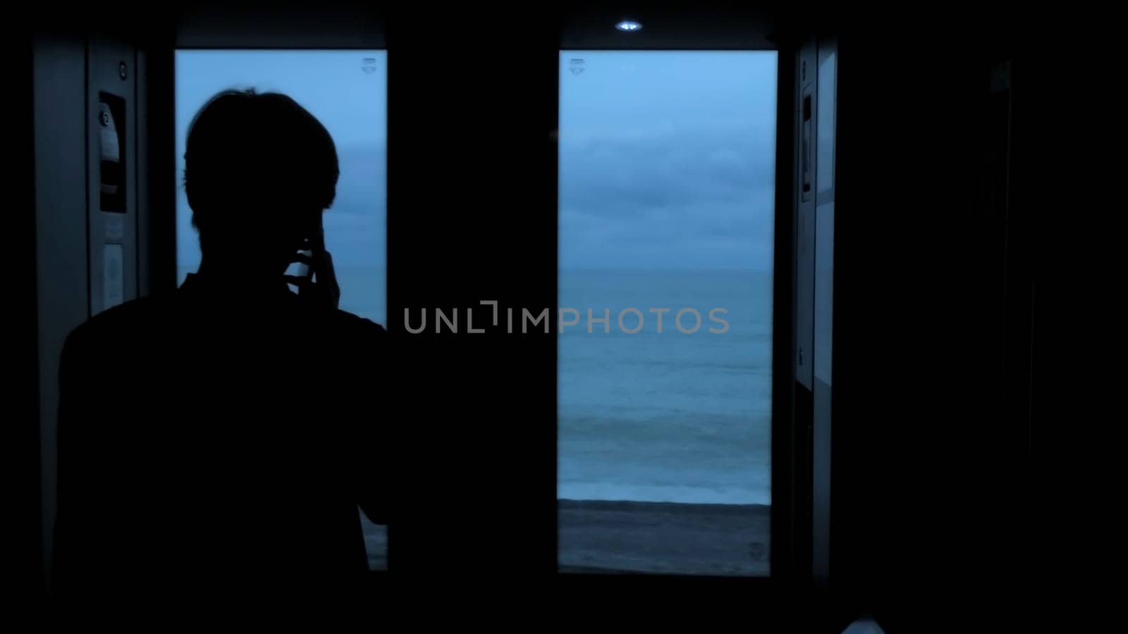 Young tourist with a smartphone looks out of the window of a moving train. Stock clip. Rear view of a male silhouette talking on phone in train