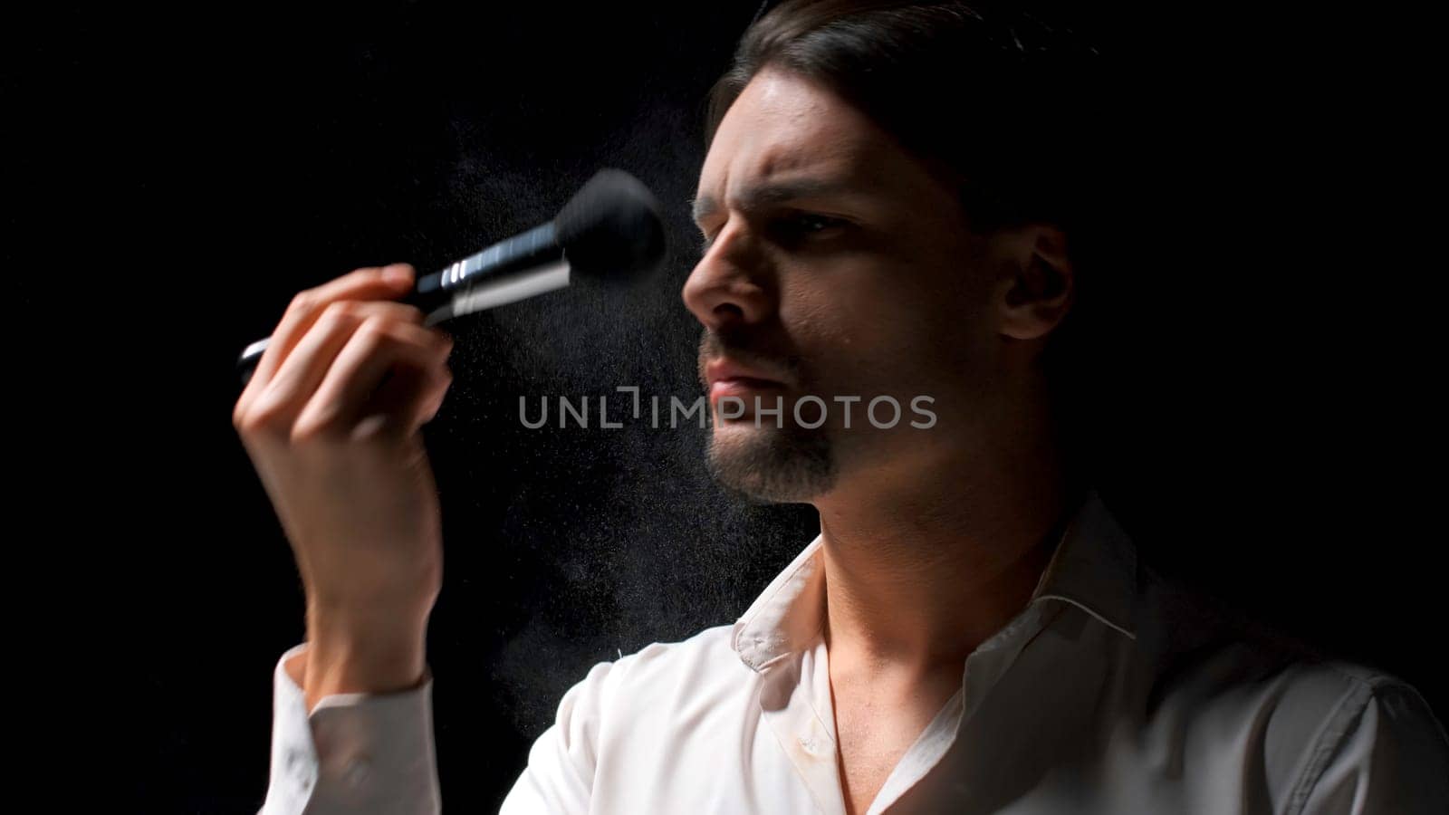 Man applies powder to his face with brush. Stock footage. Man puts powder on face on theater stage. Theatrical production with one man putting powder on face.