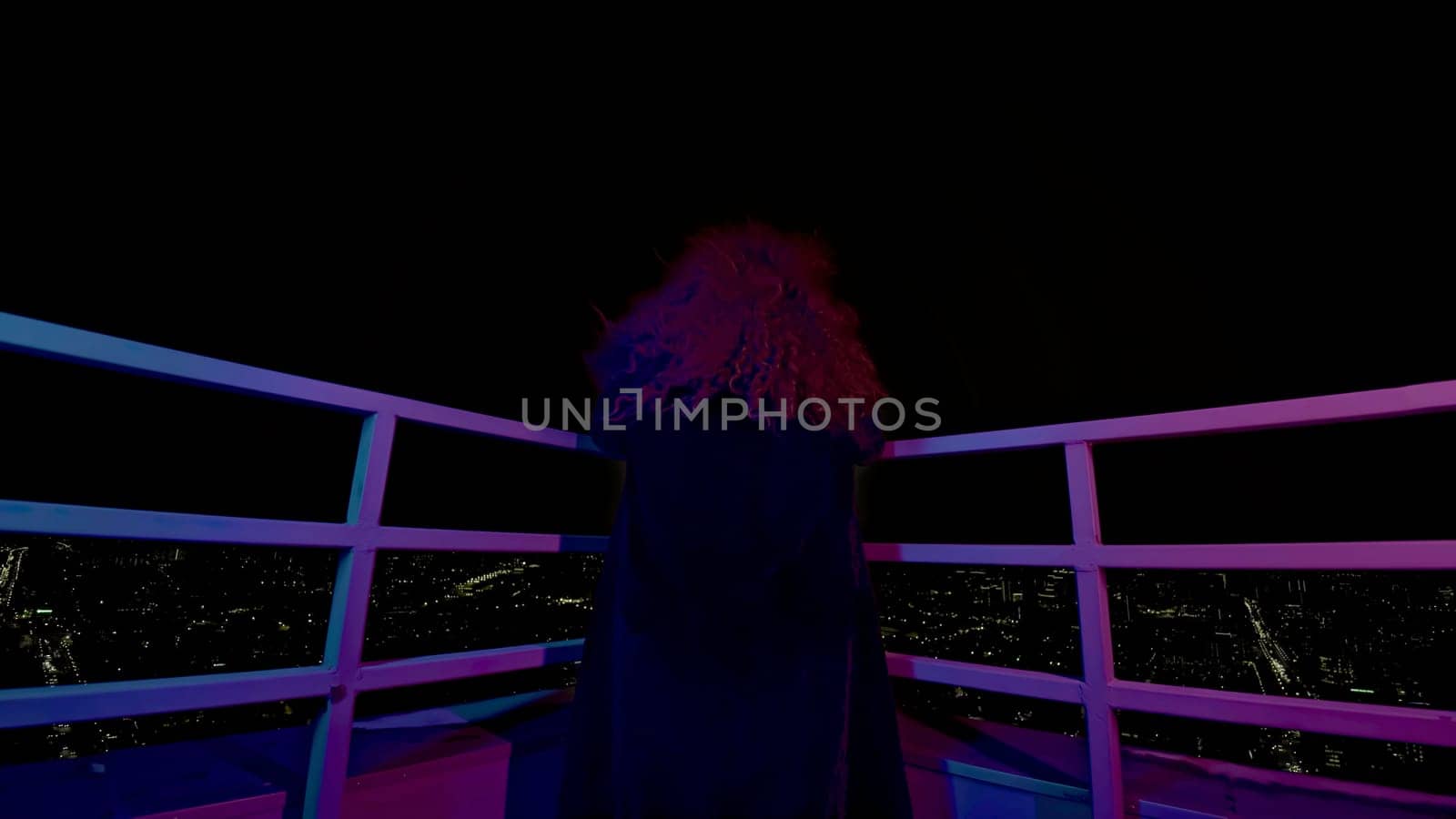 Woman on roof of high-rise building. Media. Modern witch on roof of high-rise at night. Rear view of woman on roof of high-rise at night.