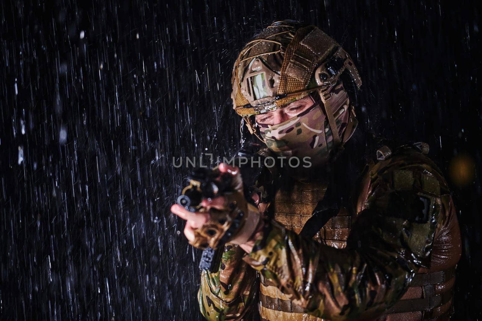 Army soldier in Combat Uniforms with an assault rifle, plate carrier and combat helmet going on a dangerous mission on a rainy night