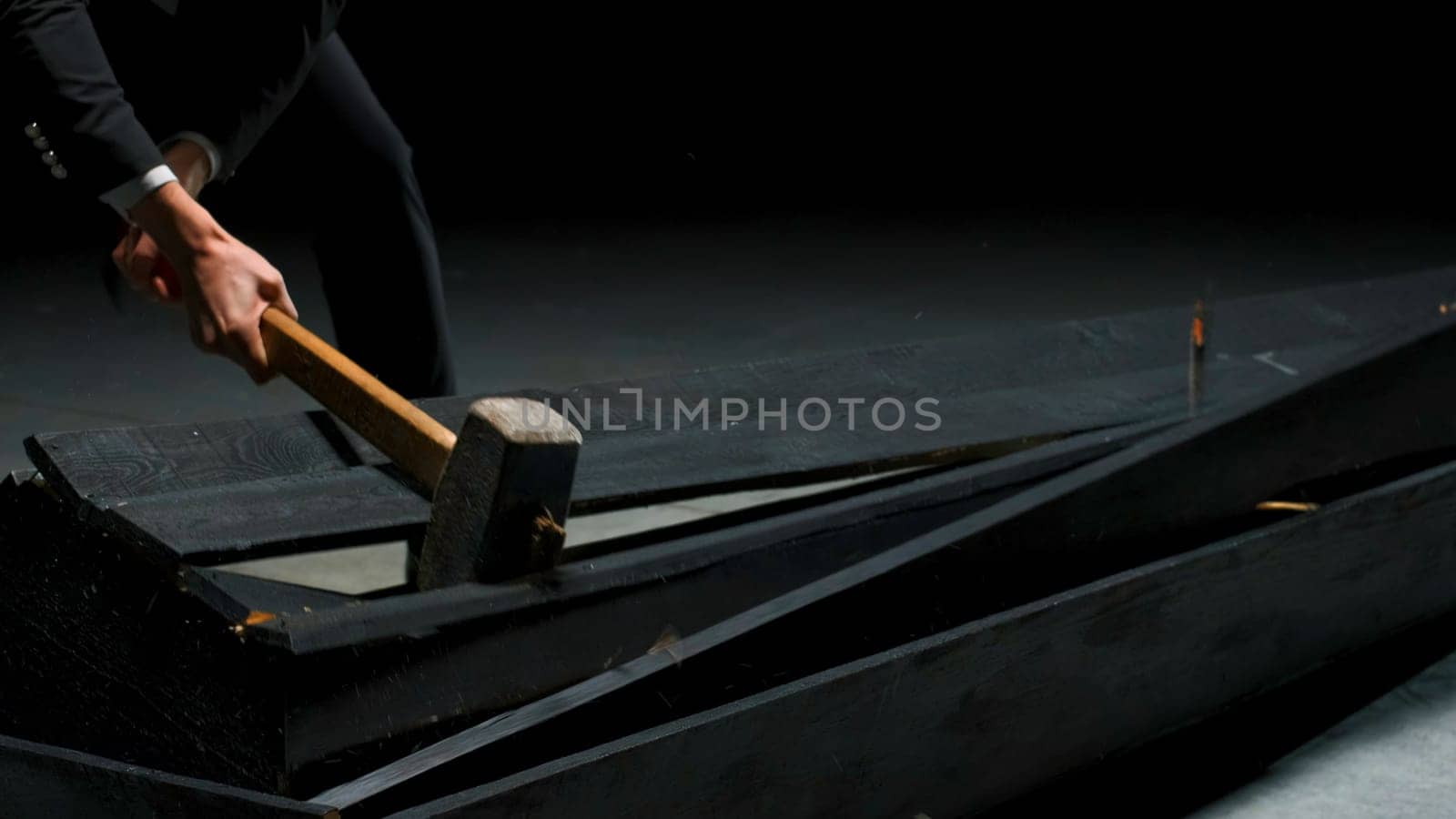 Man breaks wooden box. Stock footage. Emotional theatrical scene of destruction of coffin. Man in suit breaks coffin with hammer in emotional theatrical production.