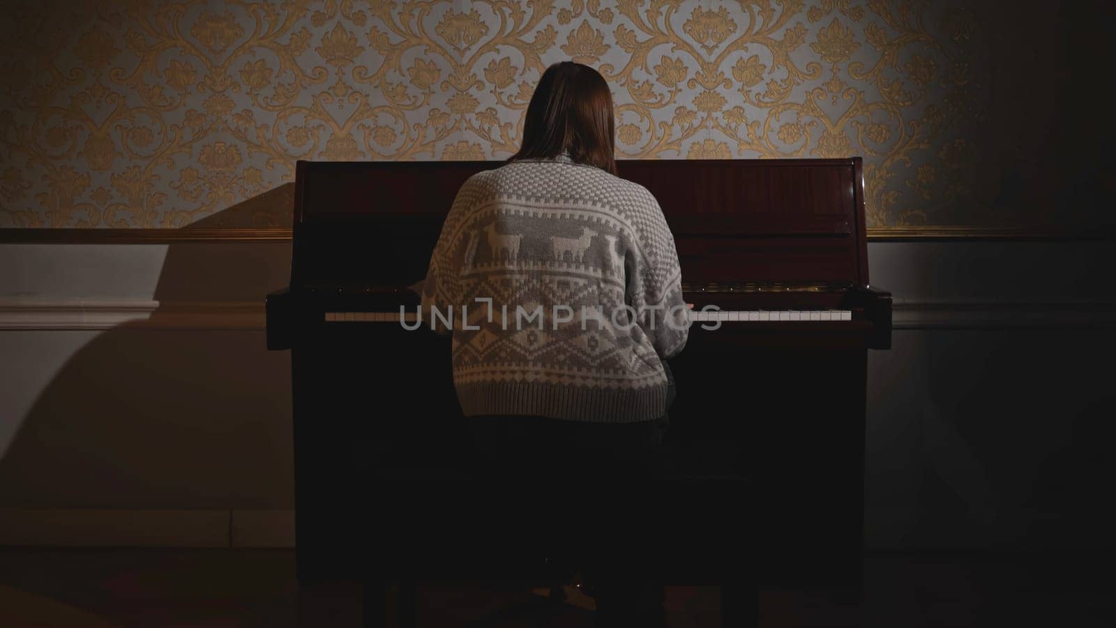 Woman starting to play piano. Media. Rear view of young woman playing piano. Woman in old sweater plays old piano.