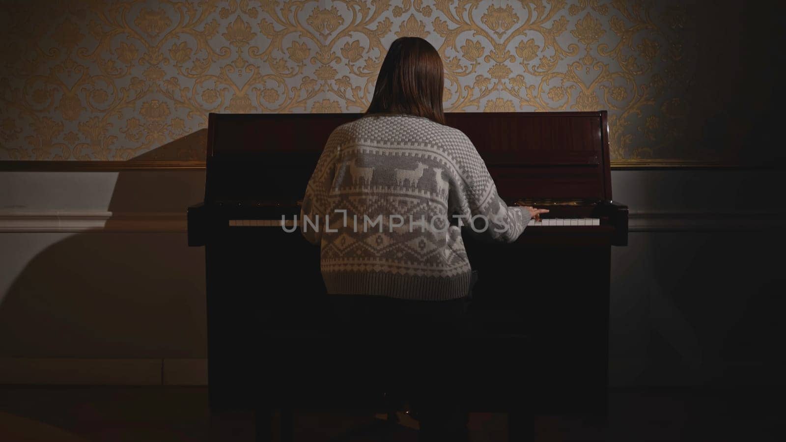 Rear view of woman playing piano. Media. Young woman is playing old piano. Granddaughter plays piano in old house.