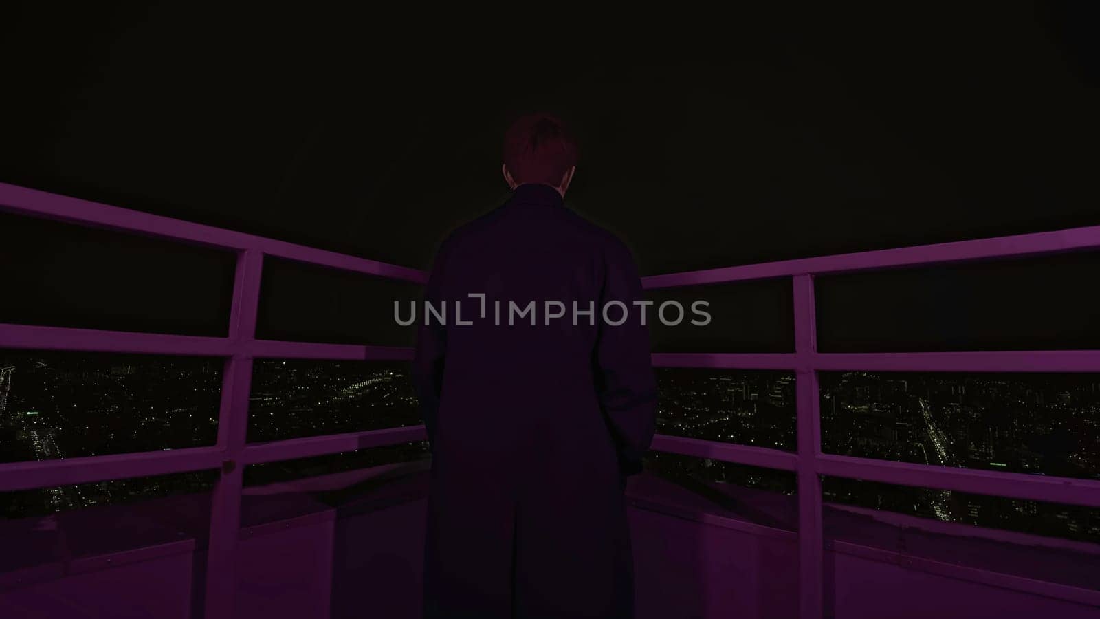 Young man stands on roof of building at night. Media. Handsome man in coat is standing on roof of high-rise building. Photo shoot of man on roof of high-rise building.