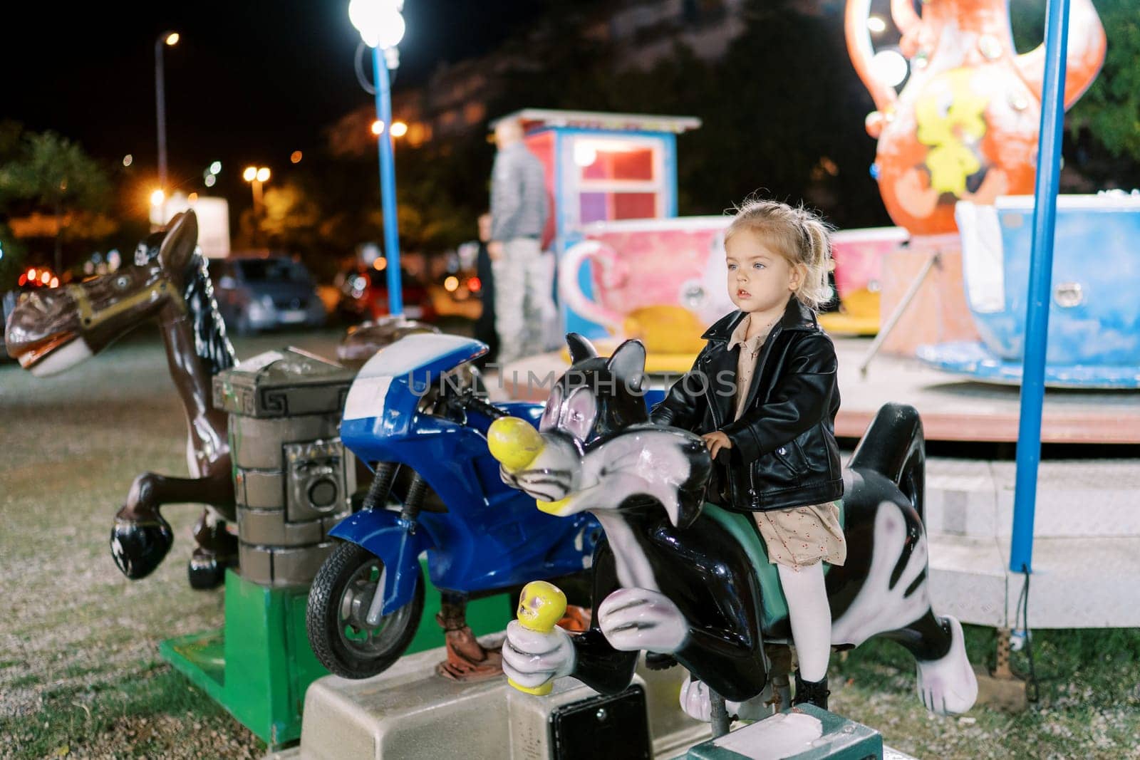 Little girl sitting on an electric cat-shaped swing at a fun fair. High quality photo