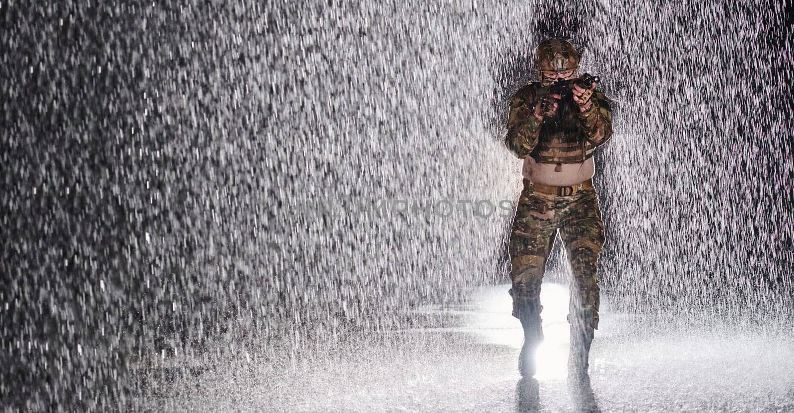 Army soldier in Combat Uniforms with an assault rifle, plate carrier and combat helmet going on a dangerous mission on a rainy night