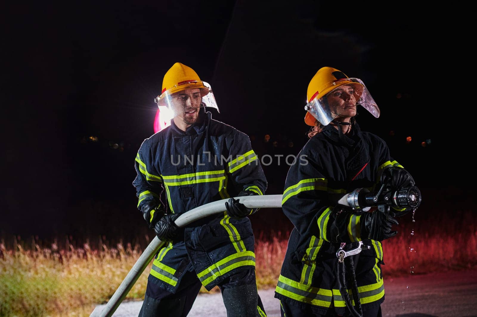 Firefighters using a water hose to eliminate a fire hazard. Team of female and male firemen in dangerous rescue mission