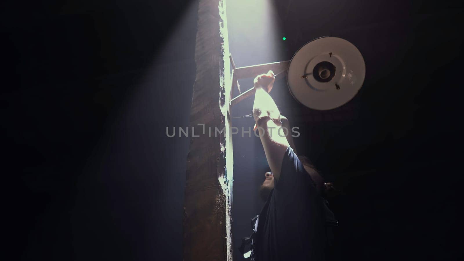 Low angle view of a male worker fixing vintage lantern on a dark background. Media. Man fixing ancient wooden street light