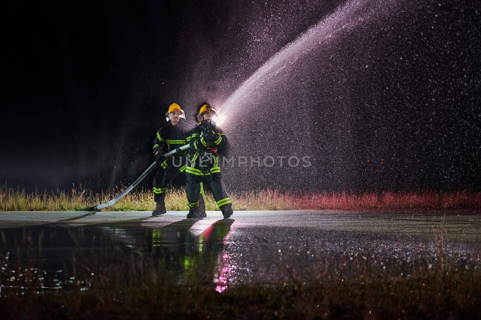 Firefighters using a water hose to eliminate a fire hazard. Team of female and male firemen in dangerous rescue mission