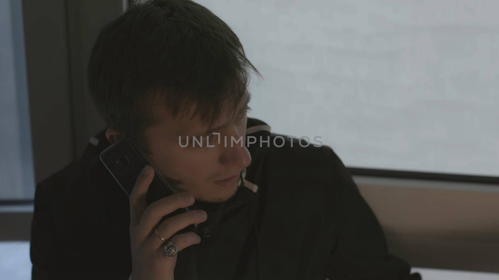 Man is calling excitedly on phone. Stock. Close-up of man calling and talking on phone. Man is making phone call on background of windows.