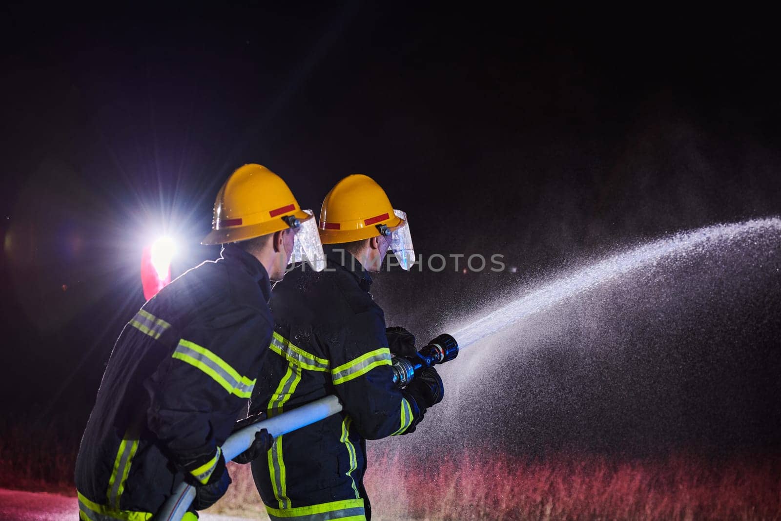 Firefighters using a water hose to eliminate a fire hazard. Team of female and male firemen in dangerous rescue mission