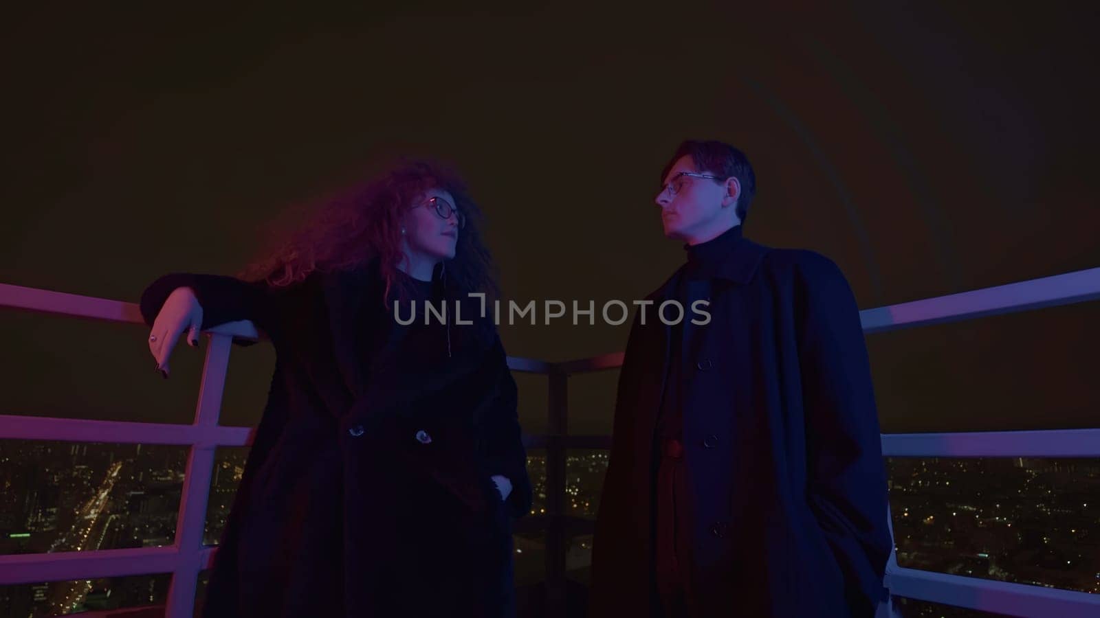 Low angle view of a couple standing on roof and looking at each other. Media. Man and woman with wild beautiful curly hair at night