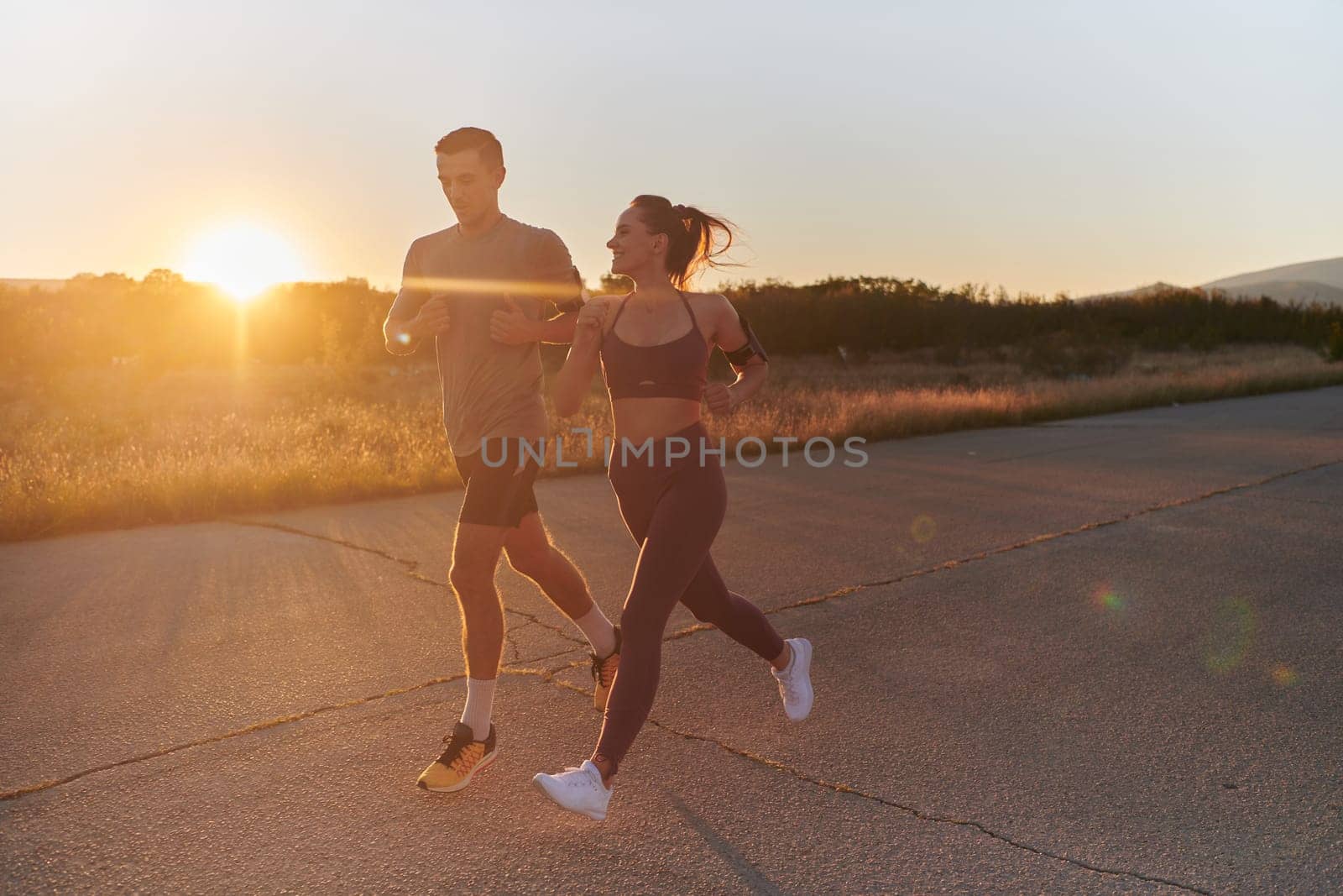 A handsome young couple running together during the early morning hours, with the mesmerizing sunrise casting a warm glow, symbolizing their shared love and vitality.