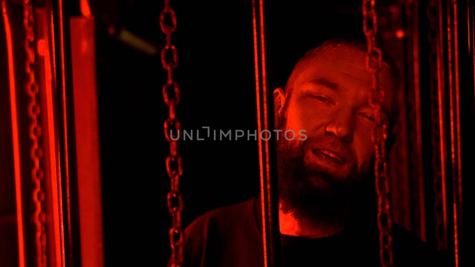 Stylish bearded man dancing by hanging chains in colorful neon light in night club. Media. Concept of rave night life