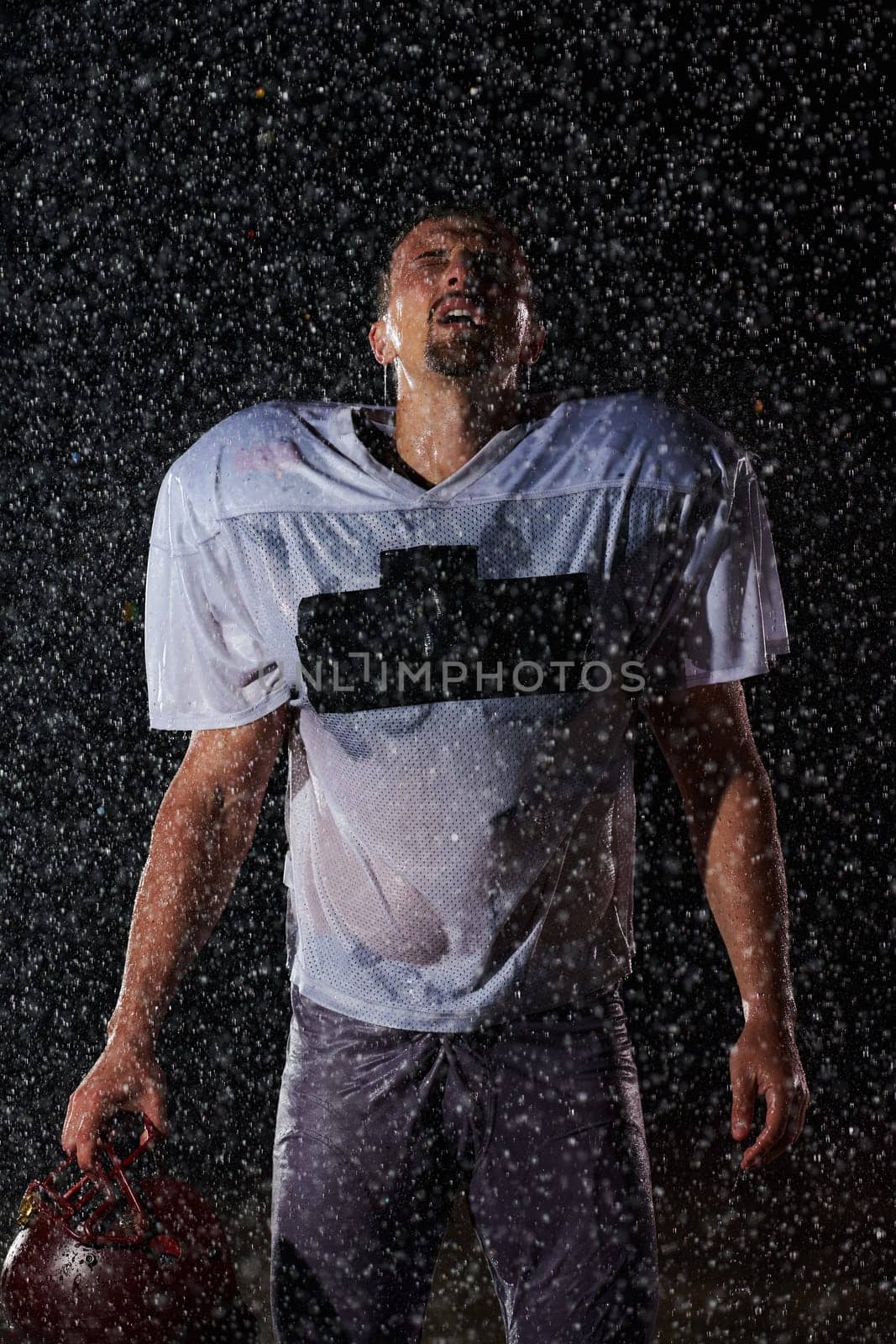 American Football Field: Lonely Athlete Warrior Standing on a Field Holds his Helmet and Ready to Play. Player Preparing to Run, Attack and Score Touchdown. Rainy Night with Dramatic Fog, Blue Light.