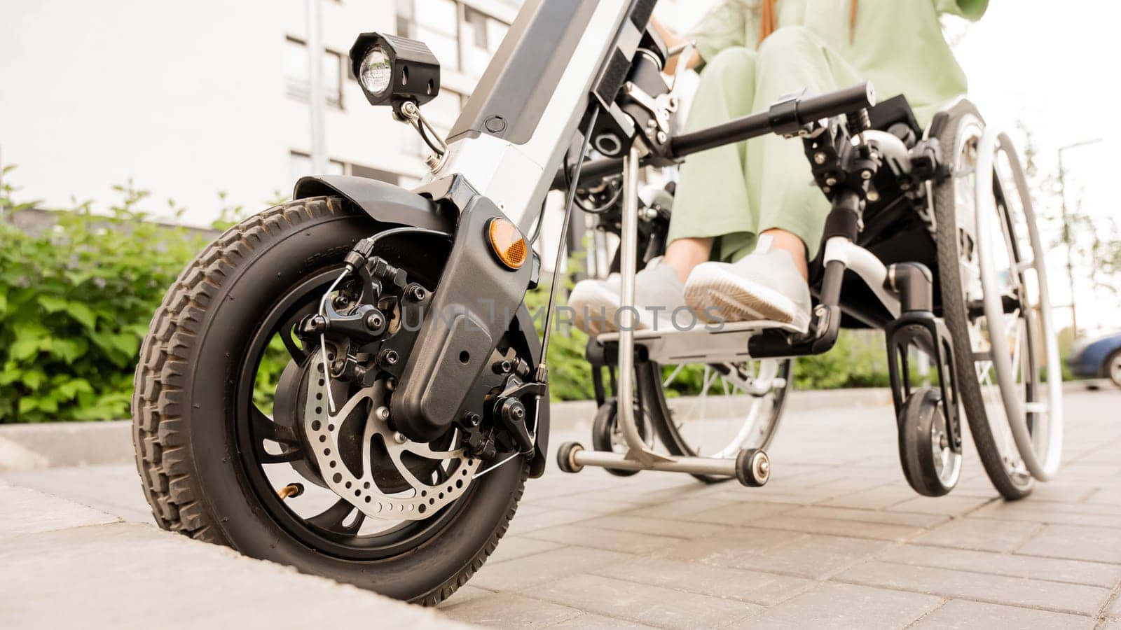 A faceless woman in a wheelchair with an assistive device for manual control. Electric handbike