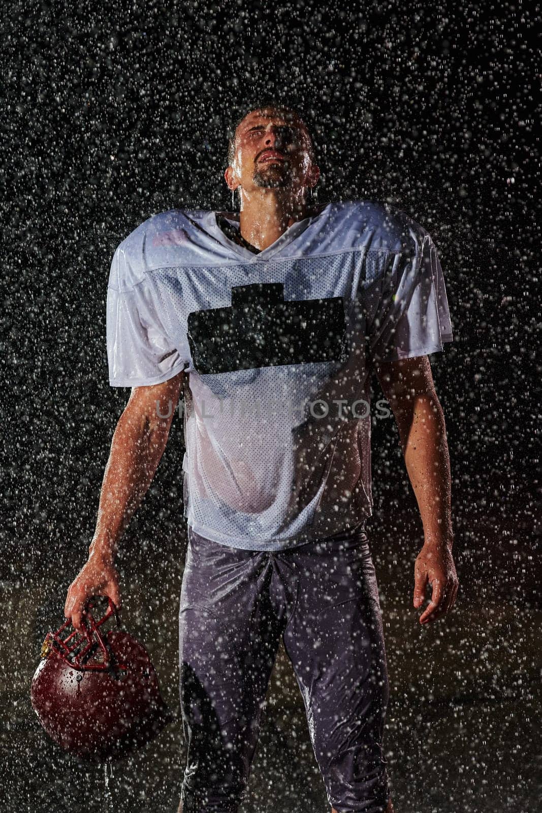 American Football Field: Lonely Athlete Warrior Standing on a Field Holds his Helmet and Ready to Play. Player Preparing to Run, Attack and Score Touchdown. Rainy Night with Dramatic Fog, Blue Light.