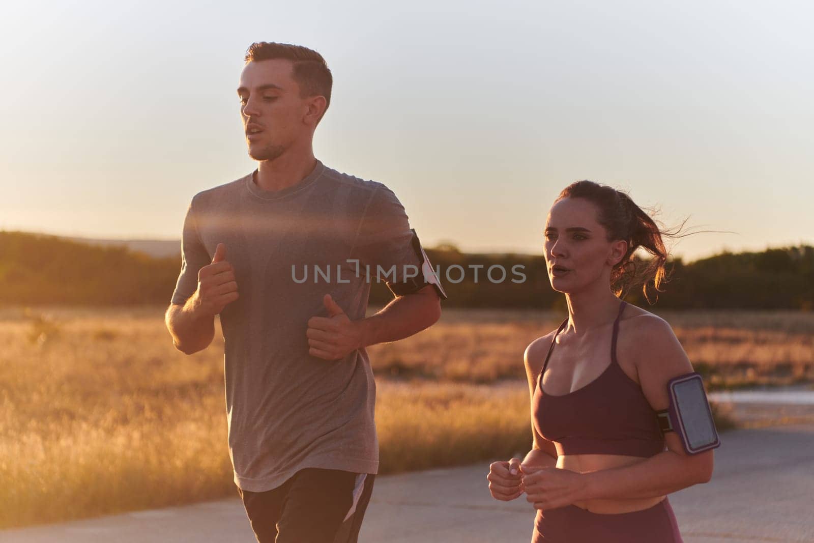 A handsome young couple running together during the early morning hours, with the mesmerizing sunrise casting a warm glow, symbolizing their shared love and vitality.