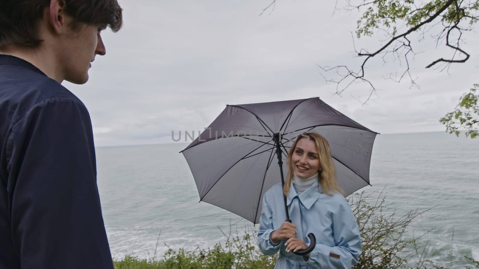 Young couple sharing a day at the beach during cold spring weather. Stock clip. Man and woman with umbrella meeting at the sea shore