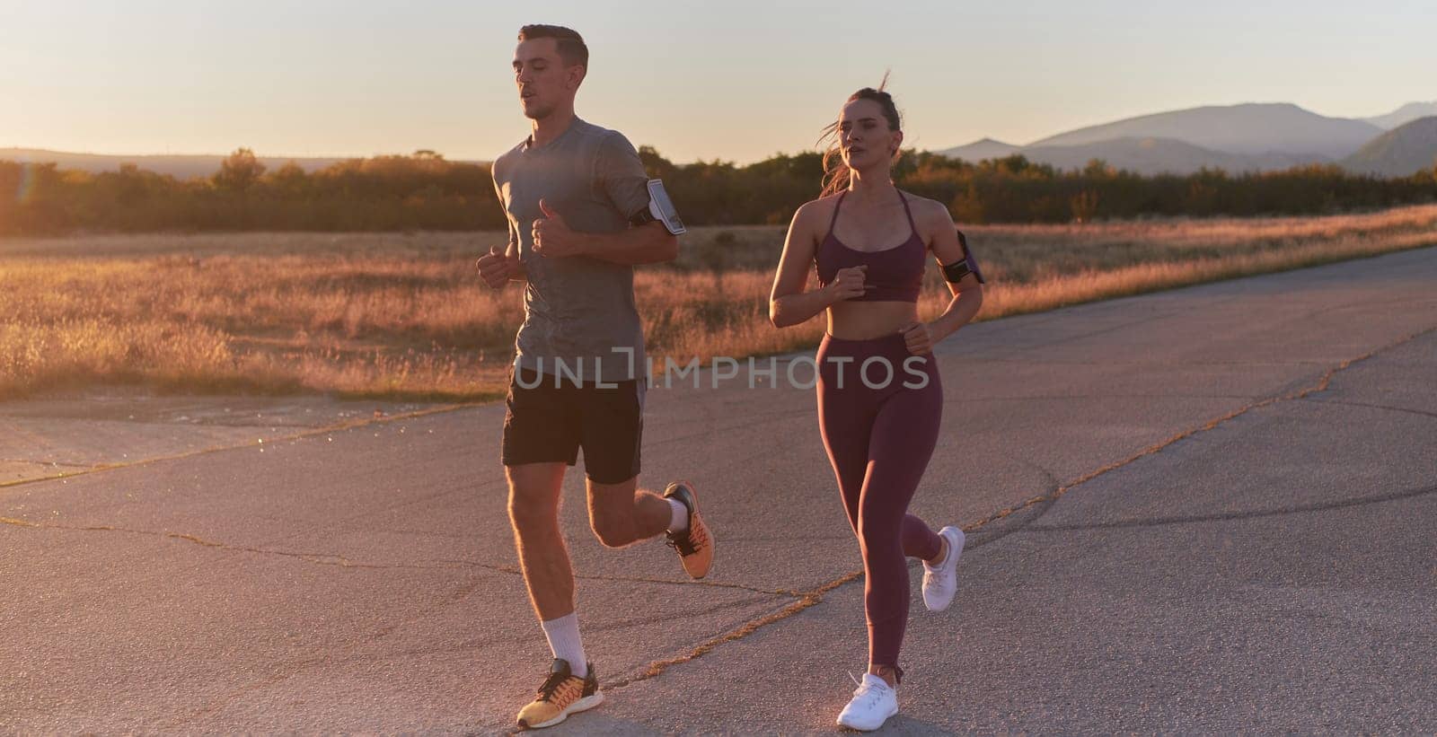 A handsome young couple running together during the early morning hours, with the mesmerizing sunrise casting a warm glow, symbolizing their shared love and vitality.