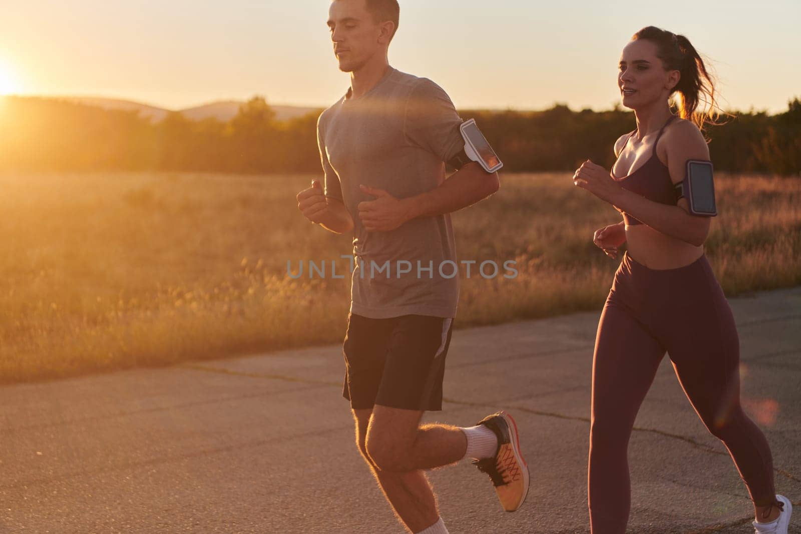 A handsome young couple running together during the early morning hours, with the mesmerizing sunrise casting a warm glow, symbolizing their shared love and vitality.