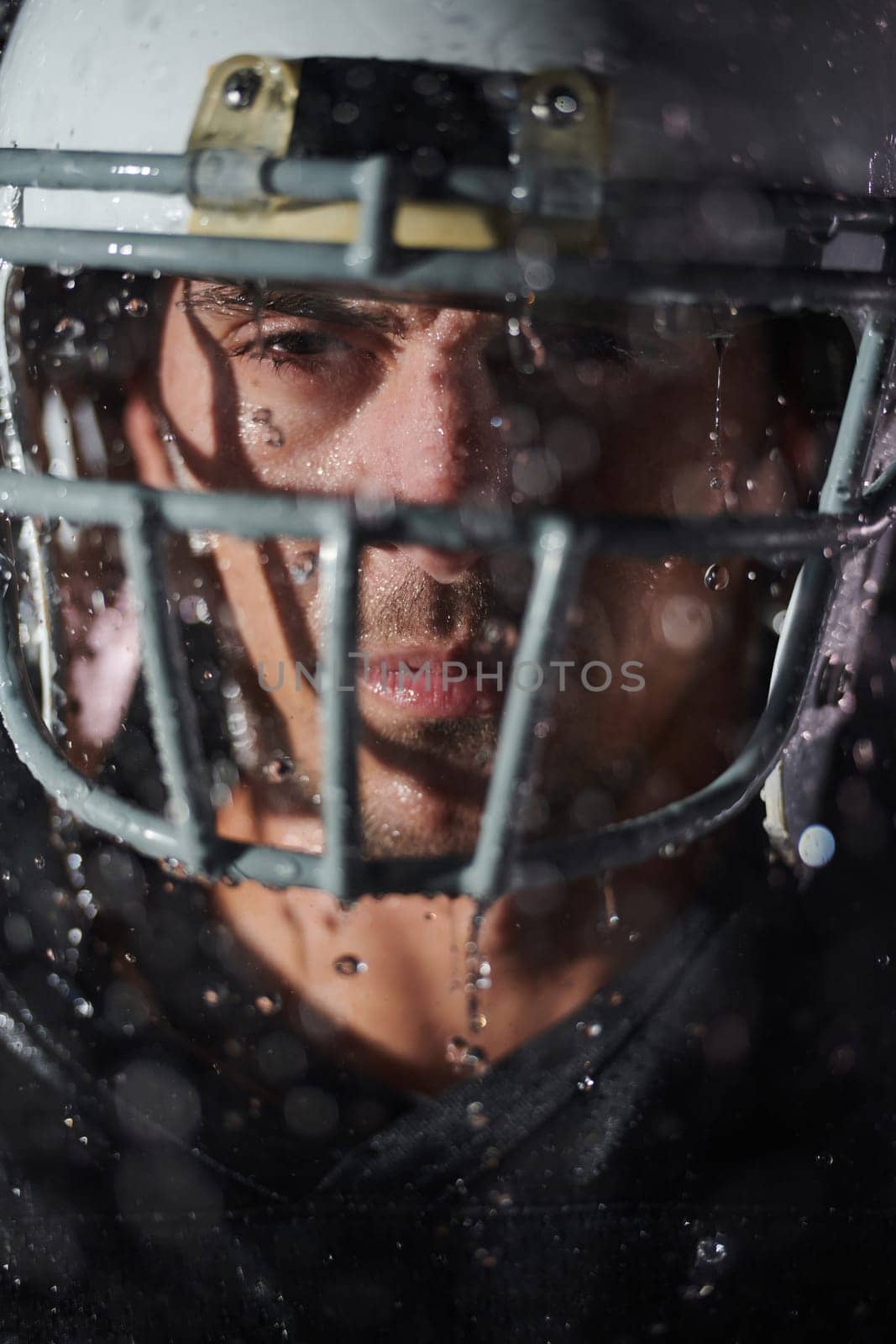 American Football Field: Lonely Athlete Warrior Standing on a Field Holds his Helmet and Ready to Play. Player Preparing to Run, Attack and Score Touchdown. Rainy Night with Dramatic Fog, Blue Light by dotshock