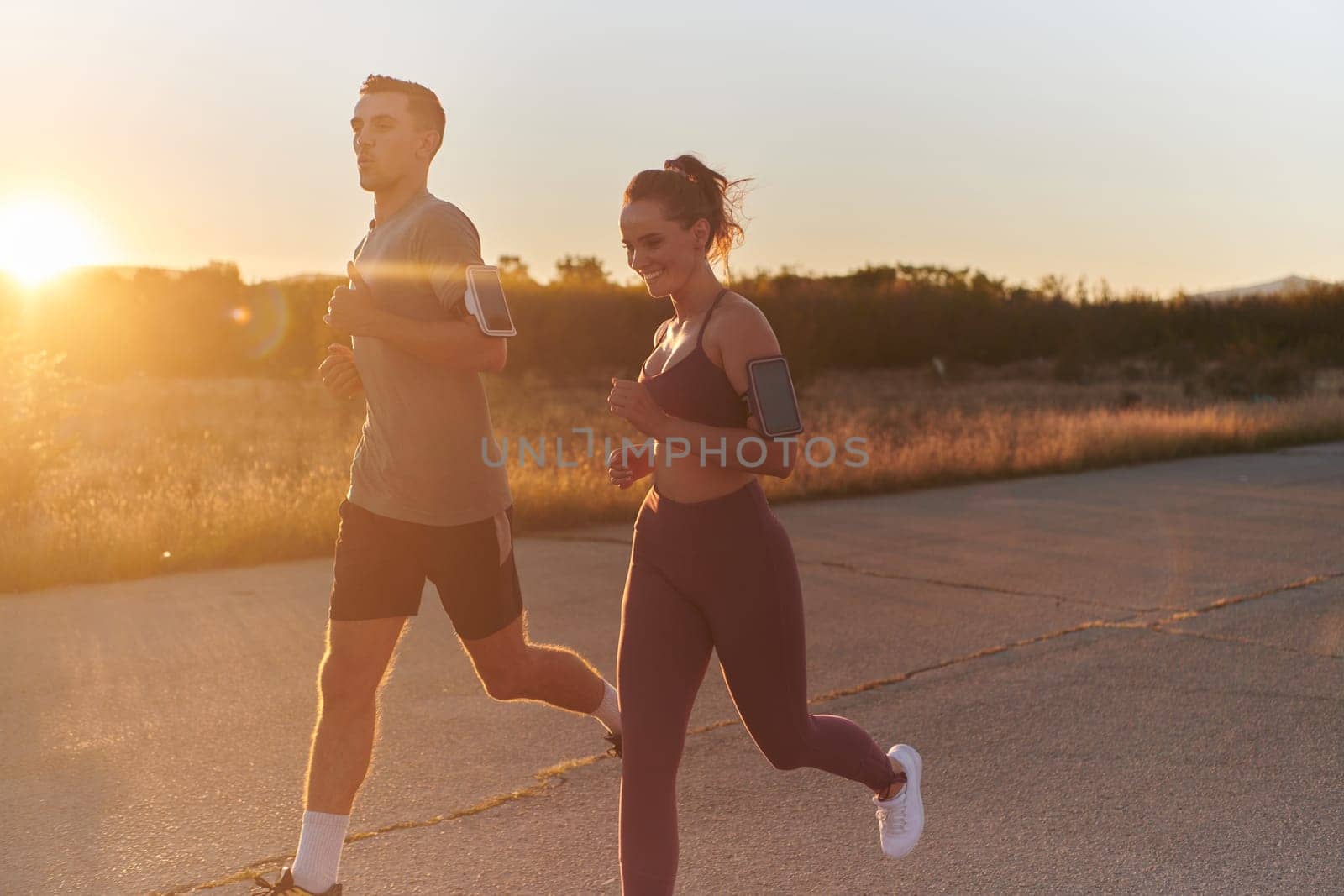A handsome young couple running together during the early morning hours, with the mesmerizing sunrise casting a warm glow, symbolizing their shared love and vitality.