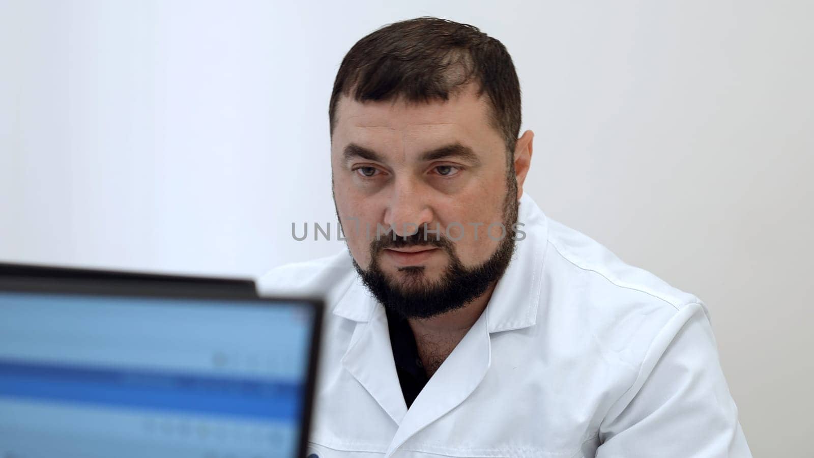 Middle aged doctor with in clinic. Clip. Bearded man in white coat looking at computer monitor