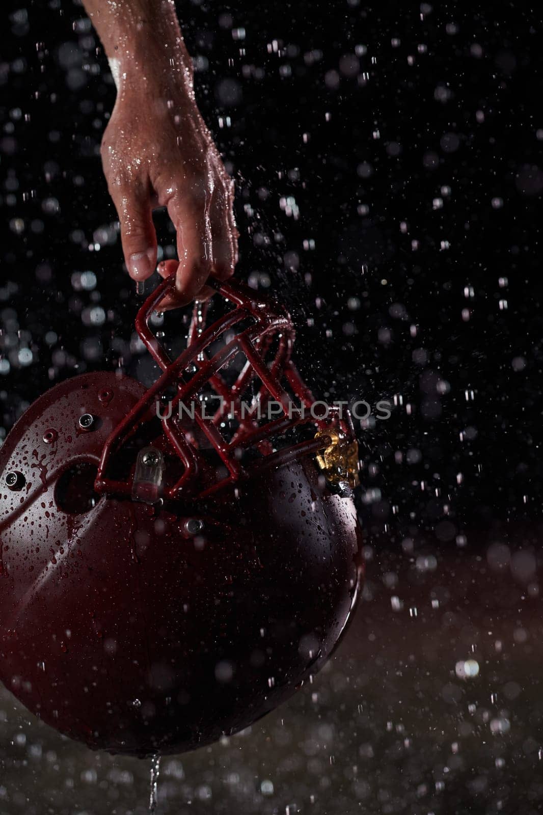 Close up of American Football Athlete Warrior Standing on a Field focus on his Helmet and Ready to Play. Player Preparing to Run, Attack and Score Touchdown. Rainy Night with Dramatic lens flare.