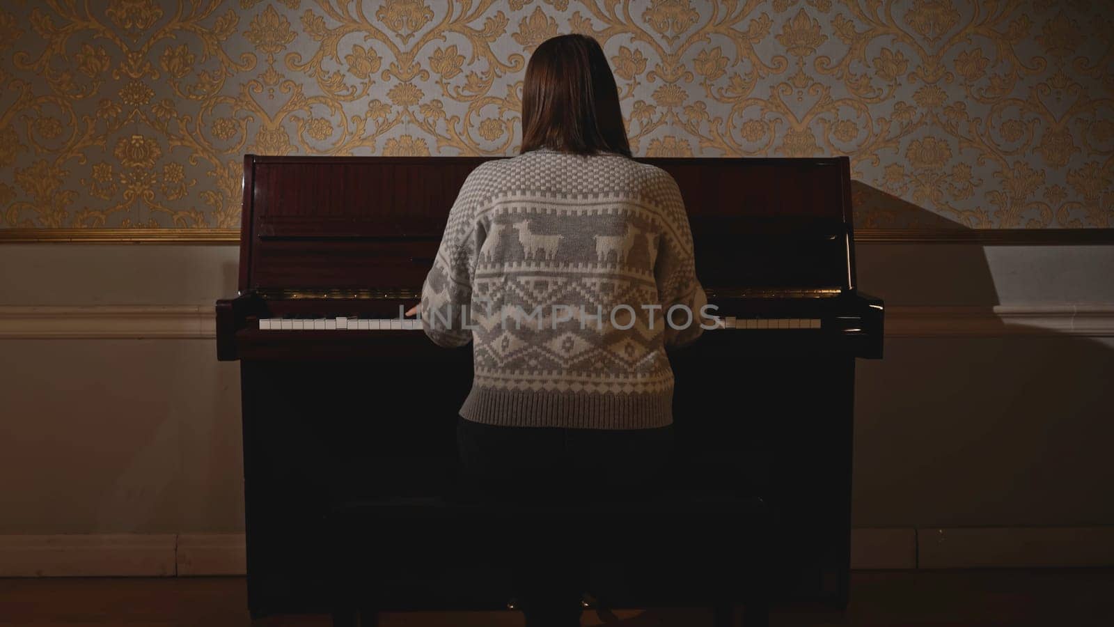 Young woman sits down to play piano. Media. Rear view of woman sitting down to play piano. Woman plays old piano.