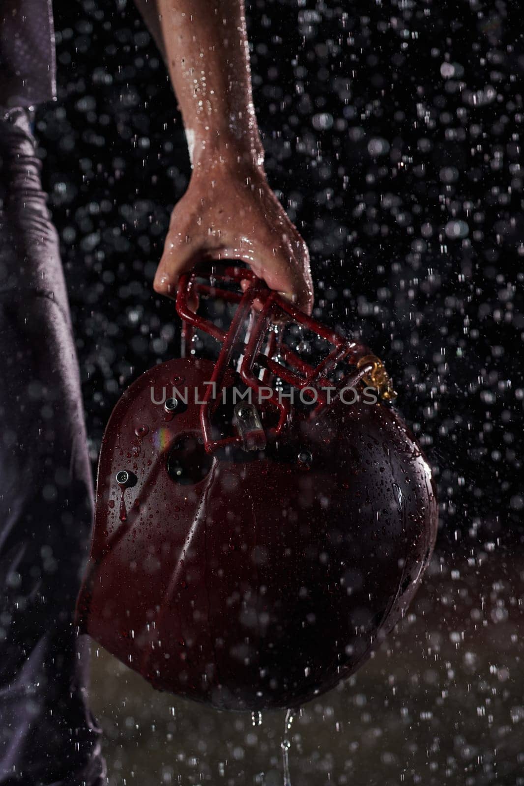 Close up of American Football Athlete Warrior Standing on a Field focus on his Helmet and Ready to Play. Player Preparing to Run, Attack and Score Touchdown. Rainy Night with Dramatic lens flare.