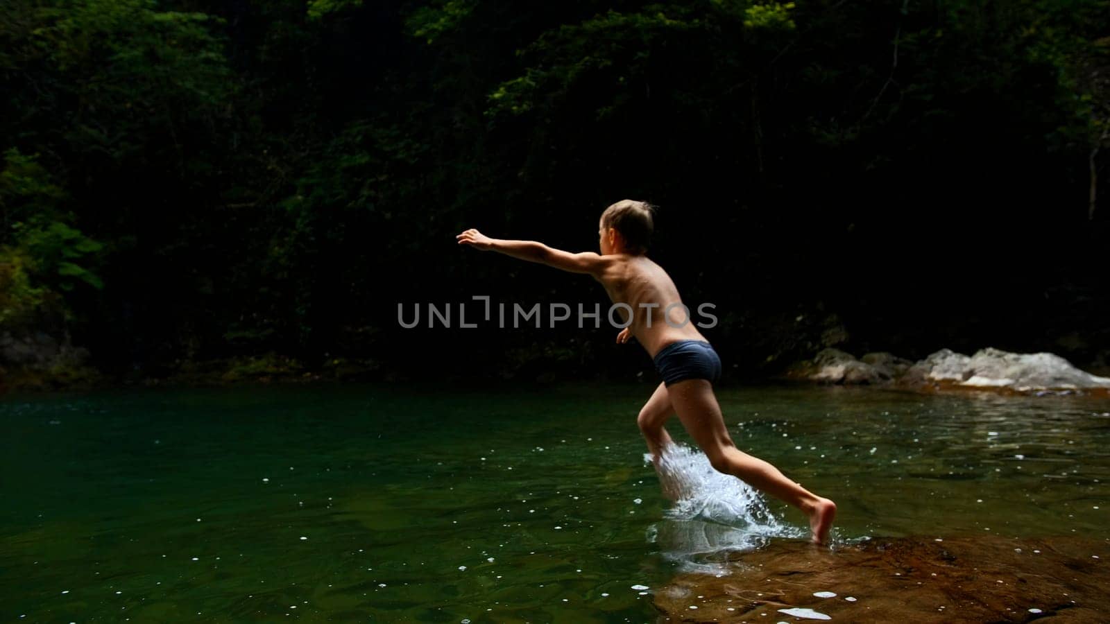 Slow motion of a boy jumping into a waterfall and natural pond. Creative. Young boy child having fun in jungles