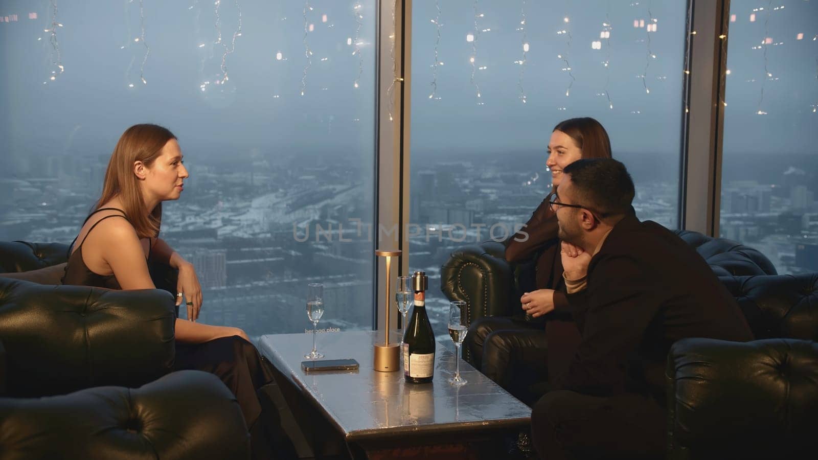 Group of friends are talking in restaurant. Media. Friends are chatting in company in restaurant. Three friends chat in restaurant on background of dark winter city.