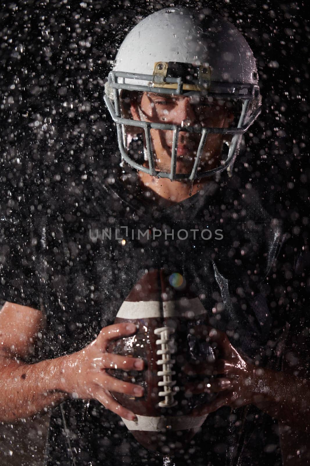 American Football Field: Lonely Athlete Warrior Standing on a Field Holds his Helmet and Ready to Play. Player Preparing to Run, Attack and Score Touchdown. Rainy Night with Dramatic Fog, Blue Light by dotshock