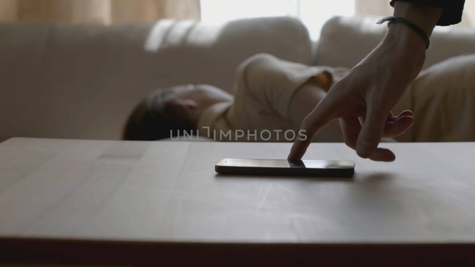 Man taking phone while woman is sleeping. Stock. Man takes phone of murdered woman. Woman is lying on couch like she was murdered and someone is taking her phone. Murder, detective, crime, drama.