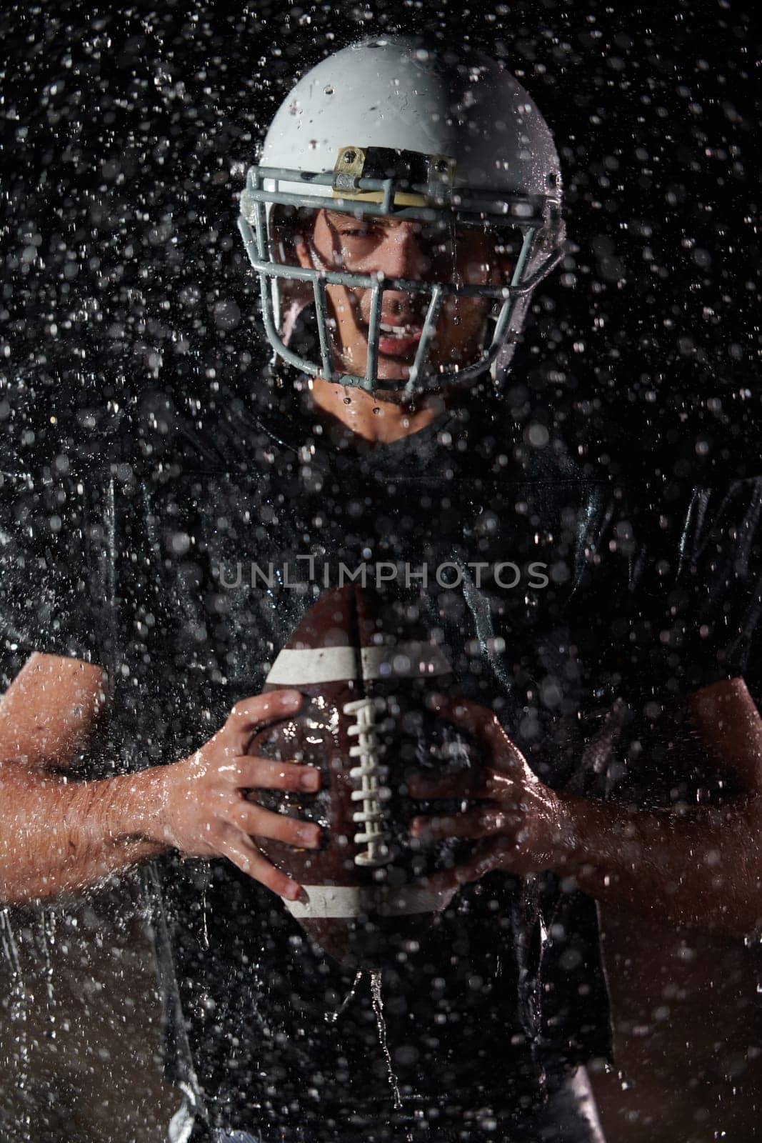 American Football Field: Lonely Athlete Warrior Standing on a Field Holds his Helmet and Ready to Play. Player Preparing to Run, Attack and Score Touchdown. Rainy Night with Dramatic Fog, Blue Light by dotshock