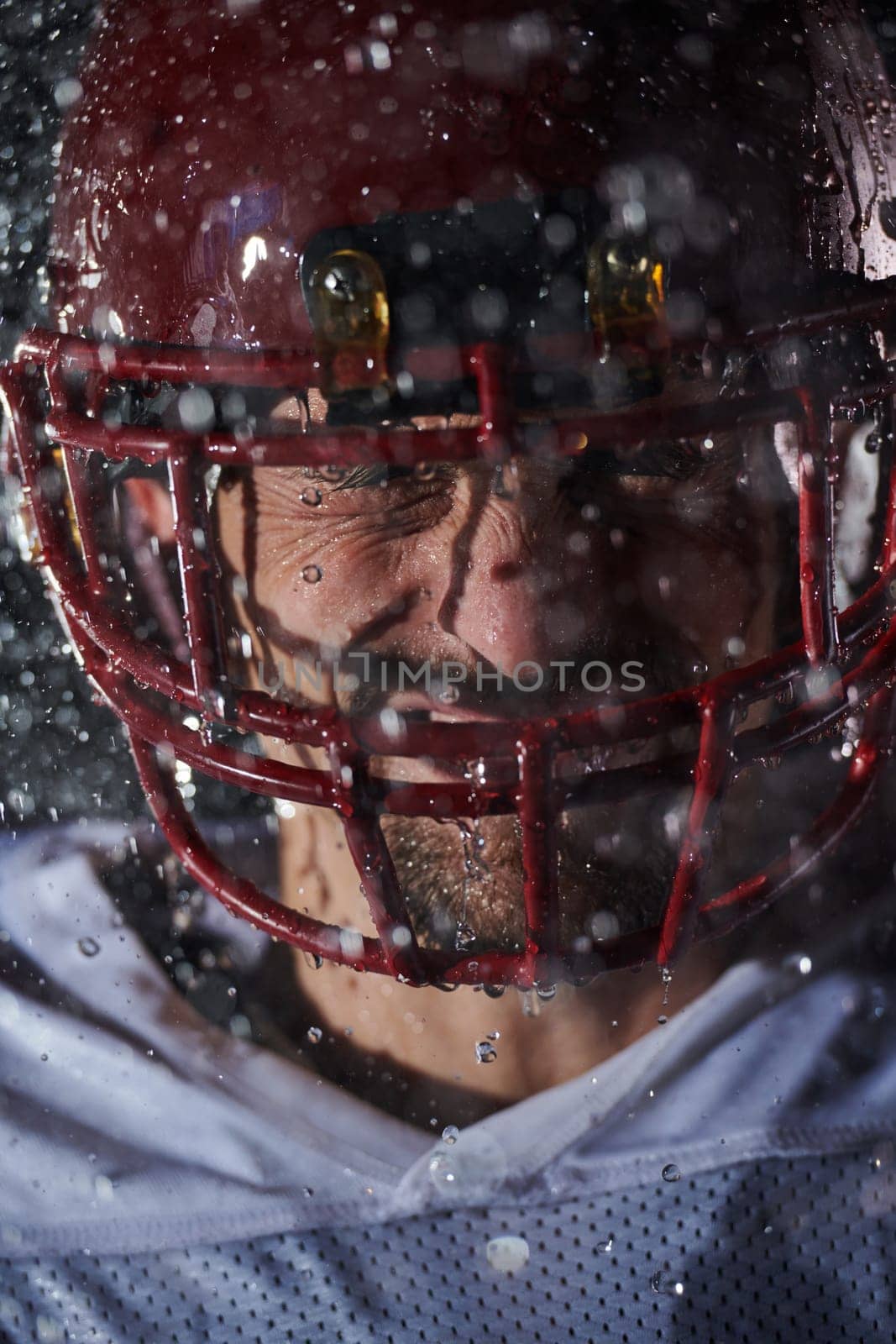 American Football Field: Lonely Athlete Warrior Standing on a Field Holds his Helmet and Ready to Play. Player Preparing to Run, Attack and Score Touchdown. Rainy Night with Dramatic Fog, Blue Light by dotshock