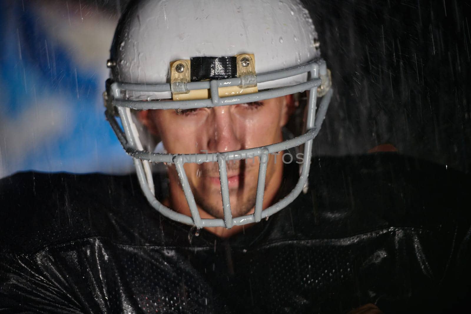 American Football Field: Lonely Athlete Warrior Standing on a Field Holds his Helmet and Ready to Play. Player Preparing to Run, Attack and Score Touchdown. Rainy Night with Dramatic Fog, Blue Light.