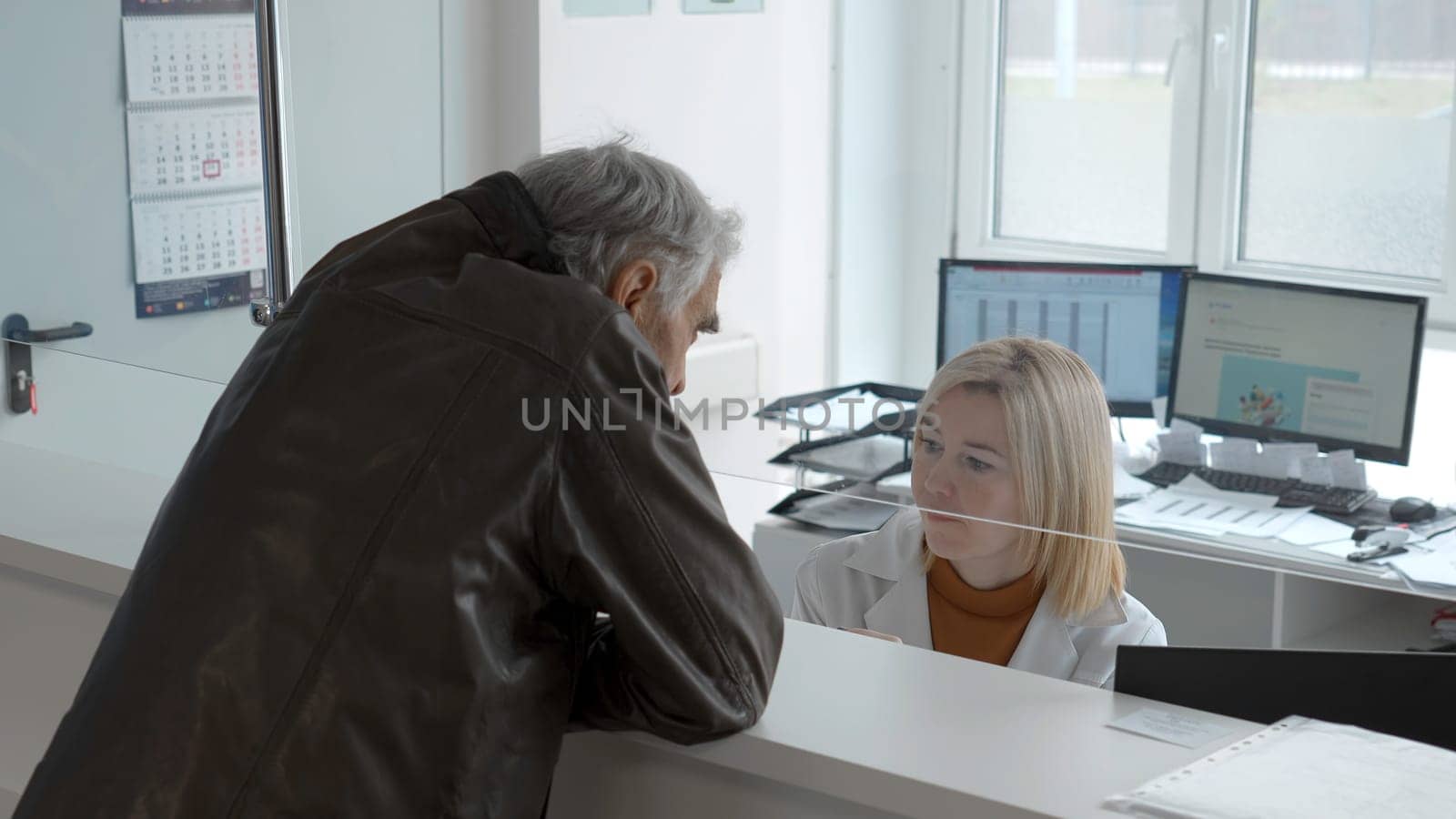 Elderly man makes appointment at reception. Clip. Elderly man makes appointment with doctor at registry. Hospital information Center for making appointment.